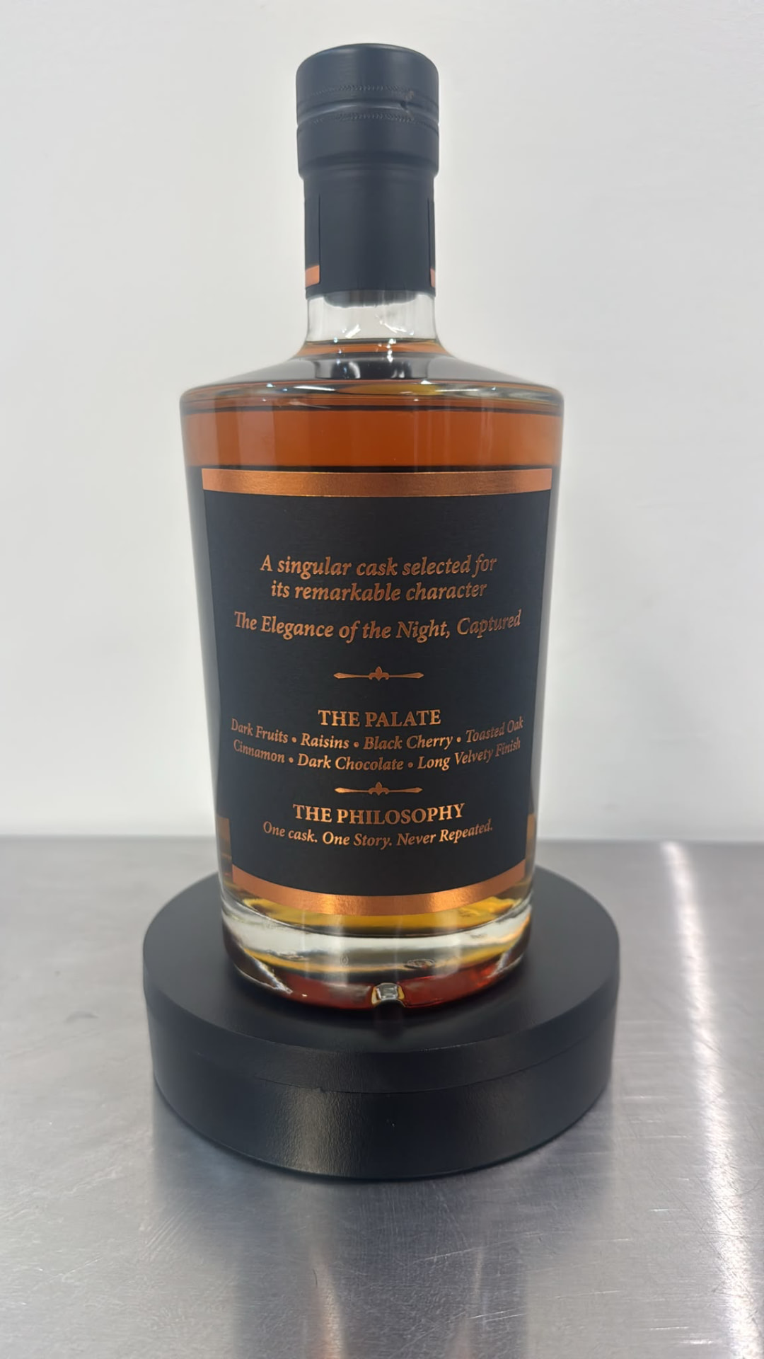 Photograph of the Noctara bottle back label listing the palate — dark fruits, raisins, black cherry, toasted oak, cinnamon, dark chocolate — and the philosophy: one cask, one story, never repeated